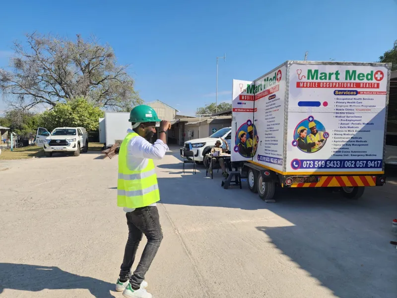 A Mart Med clinician in hard hat and reflective vest at a mine site with the mobile clinic trailer